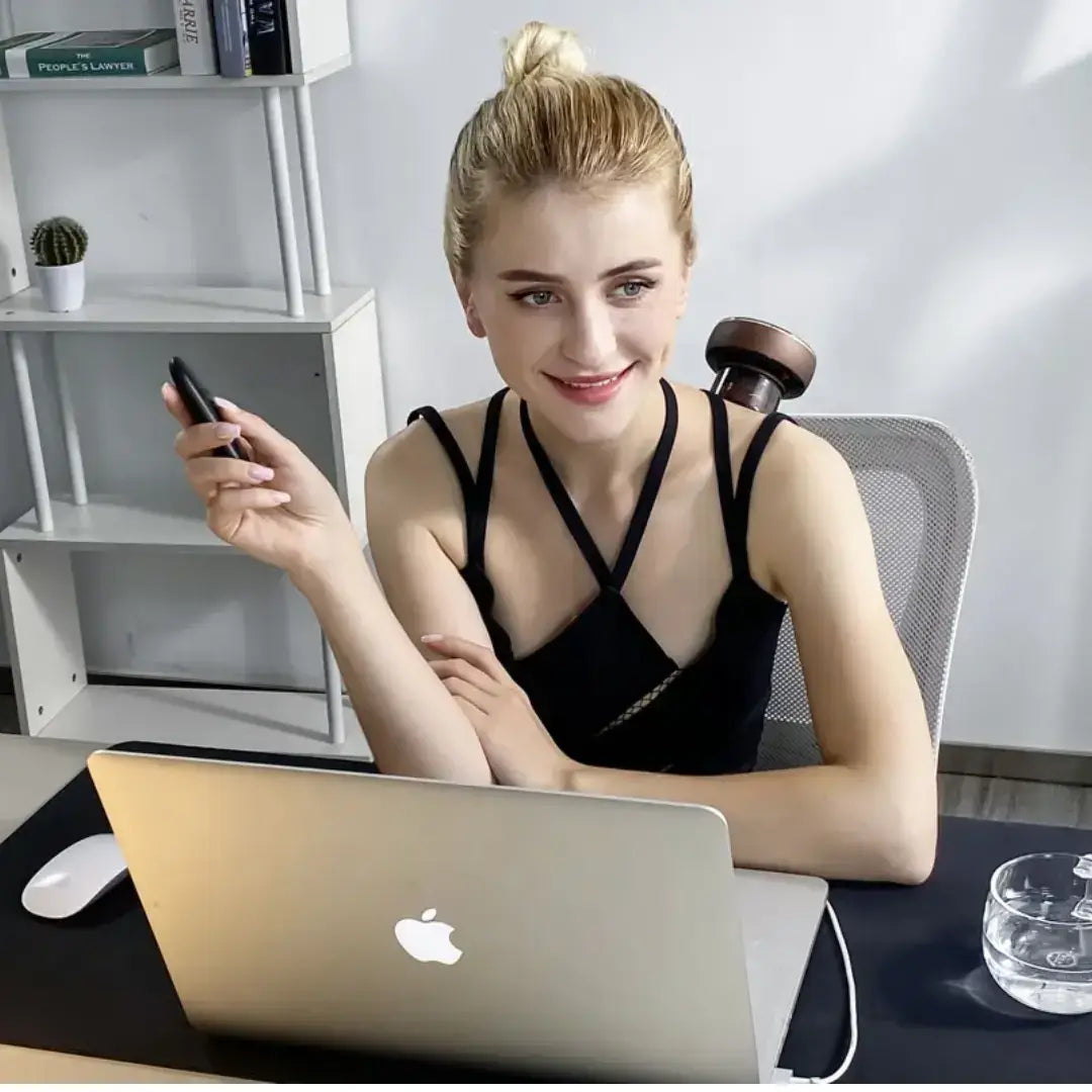 A young woman using the AcheFly Smart Cupping Device while working at her laptop in a modern office.