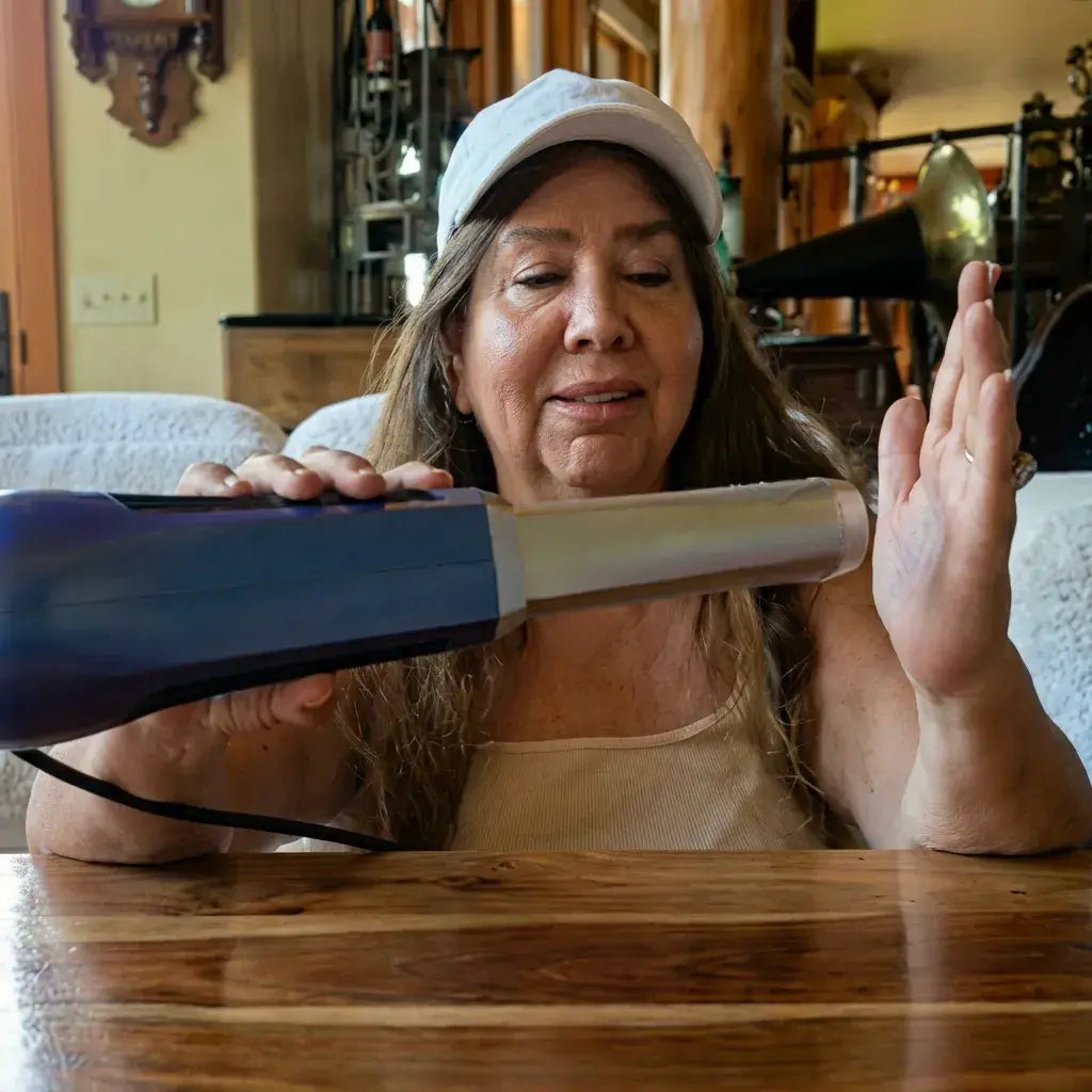 A person using the Biomax Pro Wand on their hand while seated at a wooden table.