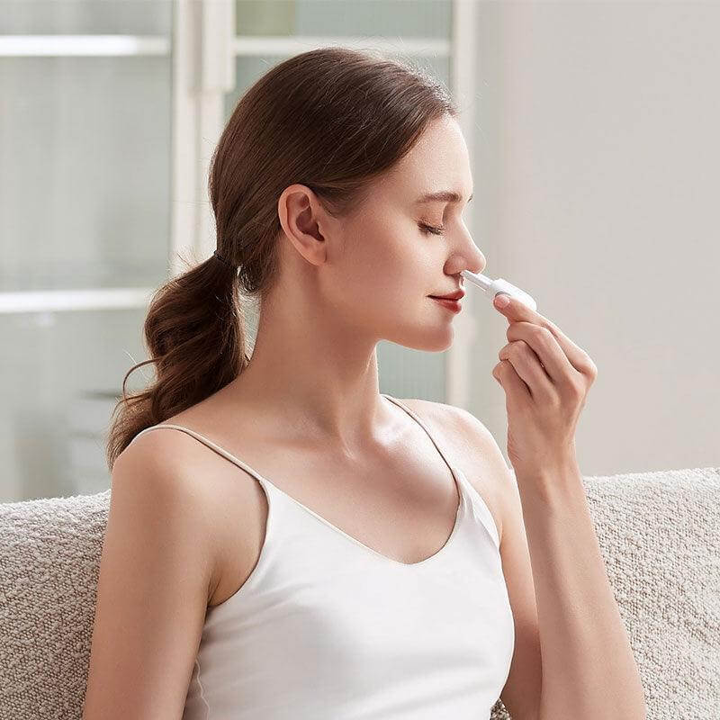 Woman using Luminose Nasal Wellness Tool for nasal comfort while sitting on a couch.