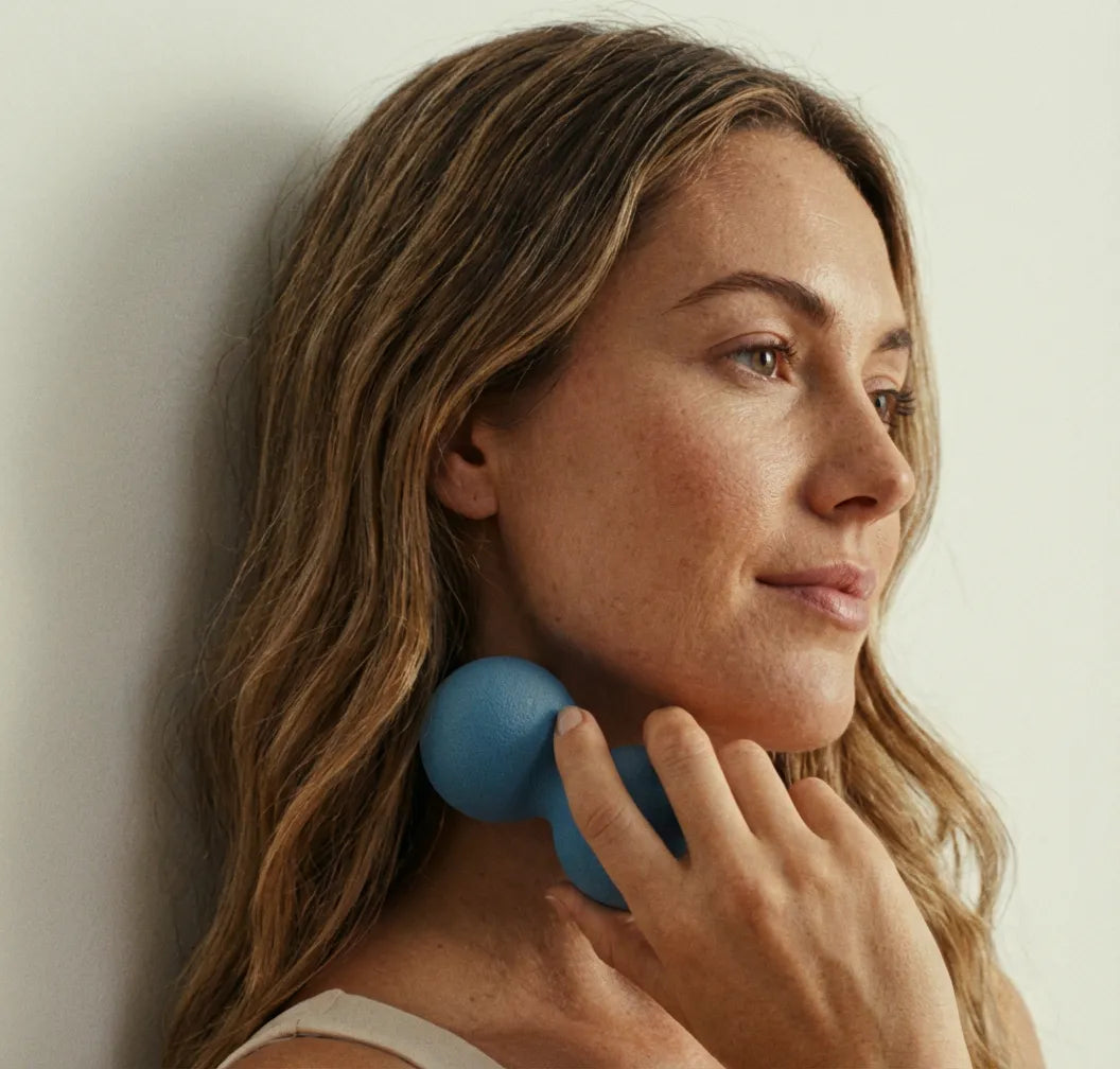 Woman using a blue massage tool on her neck, promoting relaxation and wellness.