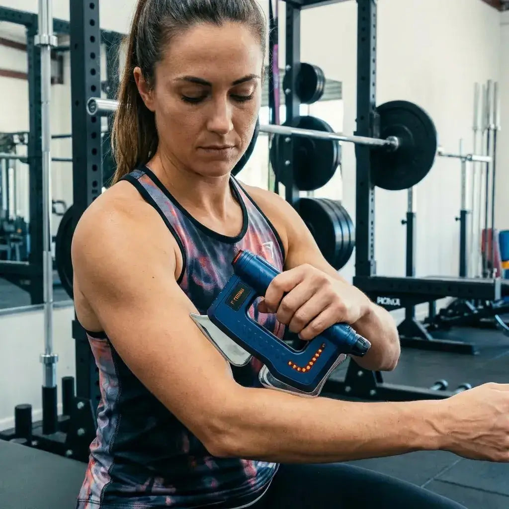 Person using the Fitdash Blade Massage Tool on their arm while in a gym setting.