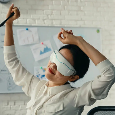 Woman in an office wearing Halipax Micro Steam Eye Cover, stretching with a pen in her hand.