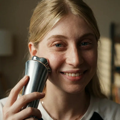 A young woman using the Polaris-II Advanced Beauty Device on her face, smiling in a cozy room.