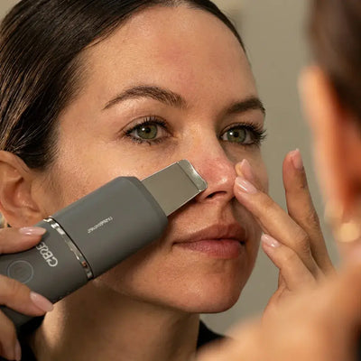 A woman using the Vellura-Gess Contour & Renew device on her nose while looking in the mirror.