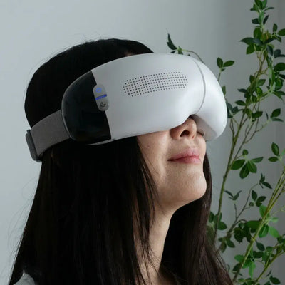 Woman wearing the Visura 3D Eye Massager, relaxing with eyes closed, surrounded by greenery.